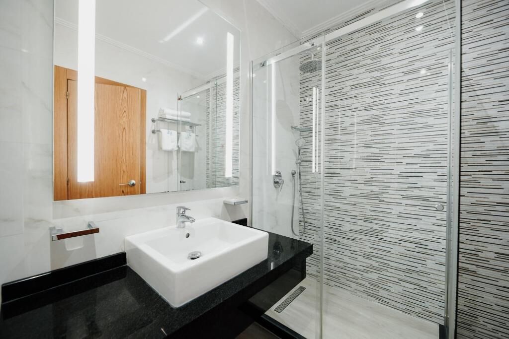 Un baño moderno con un lavamanos blanco, un mueble de madera y una cabina de ducha de vidrio.