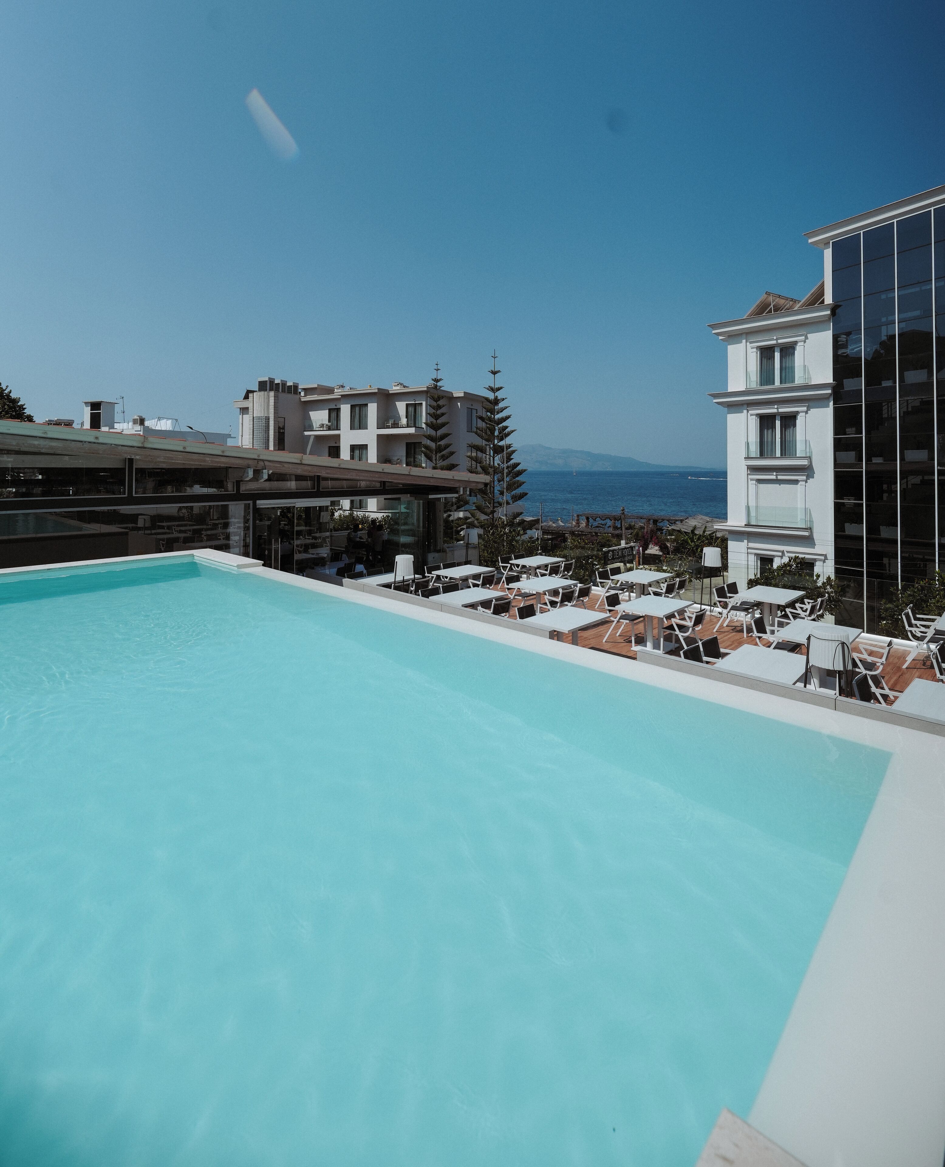 Piscina en la azotea con sillones y mesas, con vistas a la ciudad y al mar.