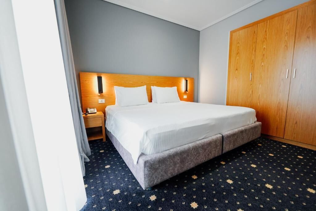 A hotel room with a bed, a wooden wardrobe, a nightstand, and a patterned carpet.