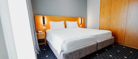 A hotel room with a bed, a wooden wardrobe, a nightstand, and a patterned carpet.