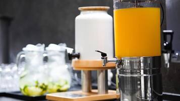 Un dispensador de jugo con un recipiente transparente y una base de madera, junto a un recipiente blanco y una jarra de vidrio.