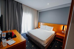 Et hotelværelse med en stor seng, et træskrivebord, et fjernsyn og et vindue med gardiner.