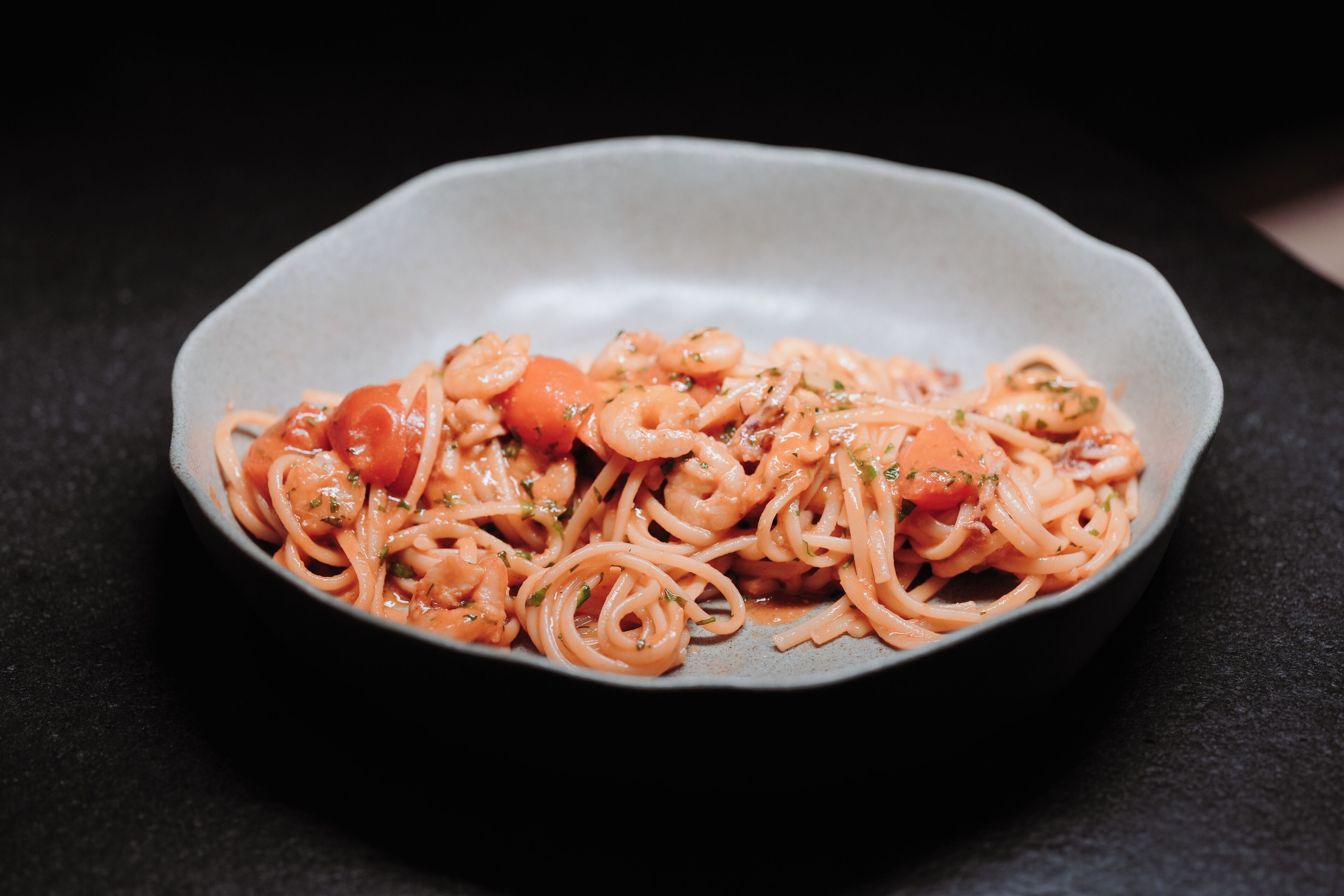 A plate of spaghetti with shrimp and tomatoes.