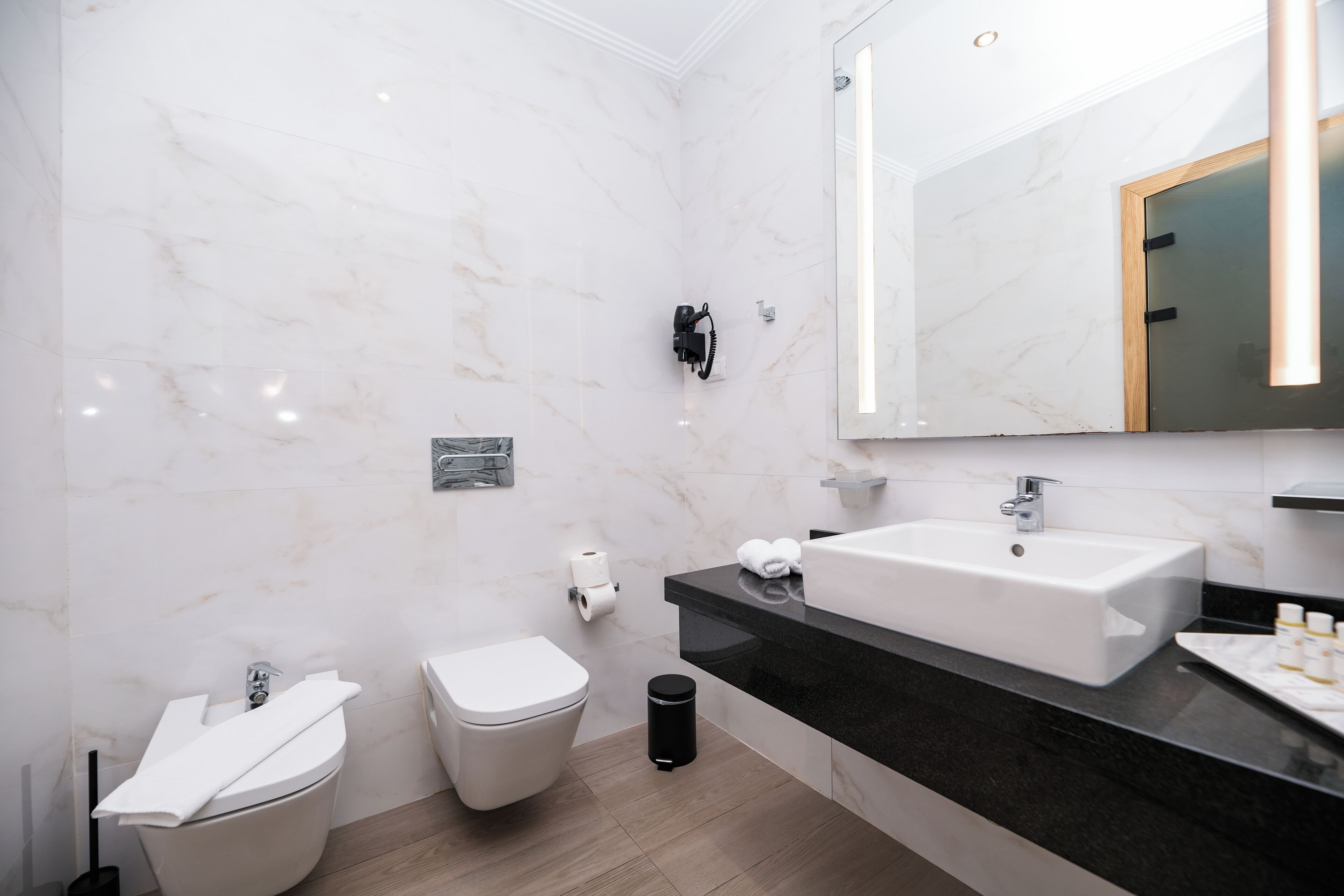 A modern bathroom with a white marble wall, a black countertop, a white sink, and a toilet.