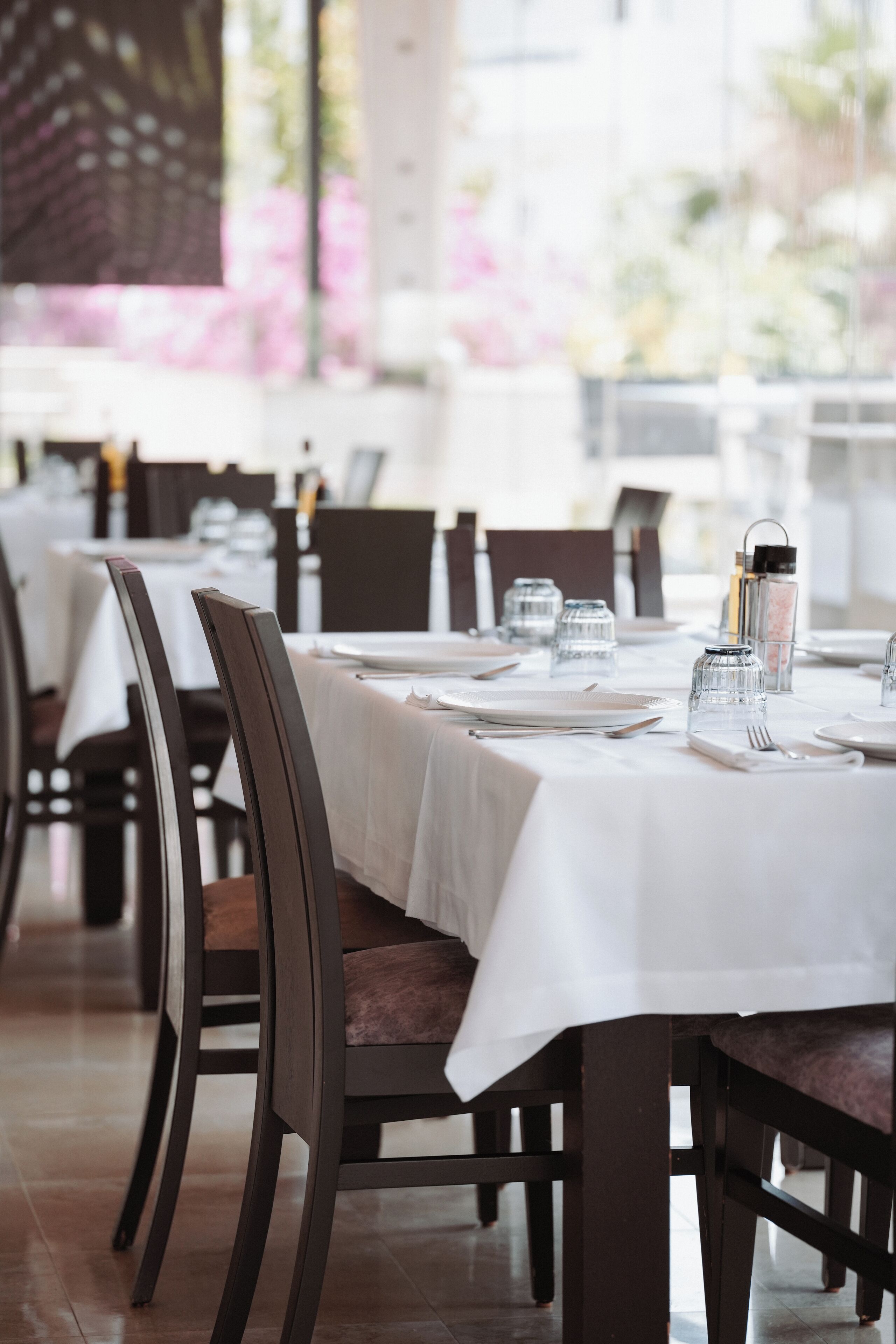 A restaurant with tables set for dining, featuring dark wooden chairs and white tablecloths.