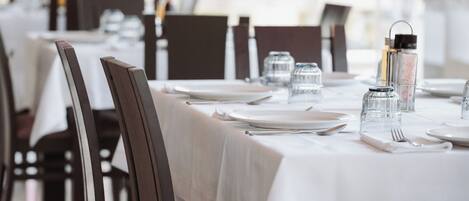 A restaurant with tables set for dining, featuring dark wooden chairs and white tablecloths.