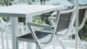 A modern outdoor seating area with a white table and chairs, surrounded by glass walls and greenery.