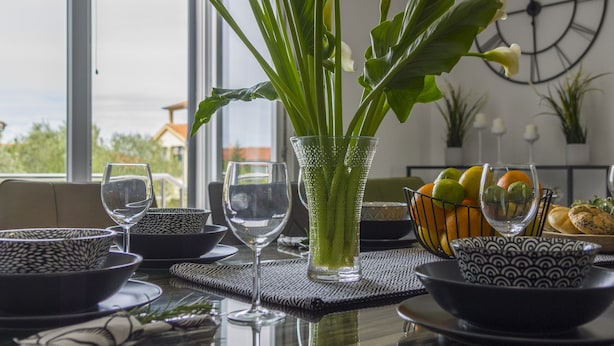 Et moderne spiseområde med et glasbord, krystalklare glas og en vase med hvide blomster.