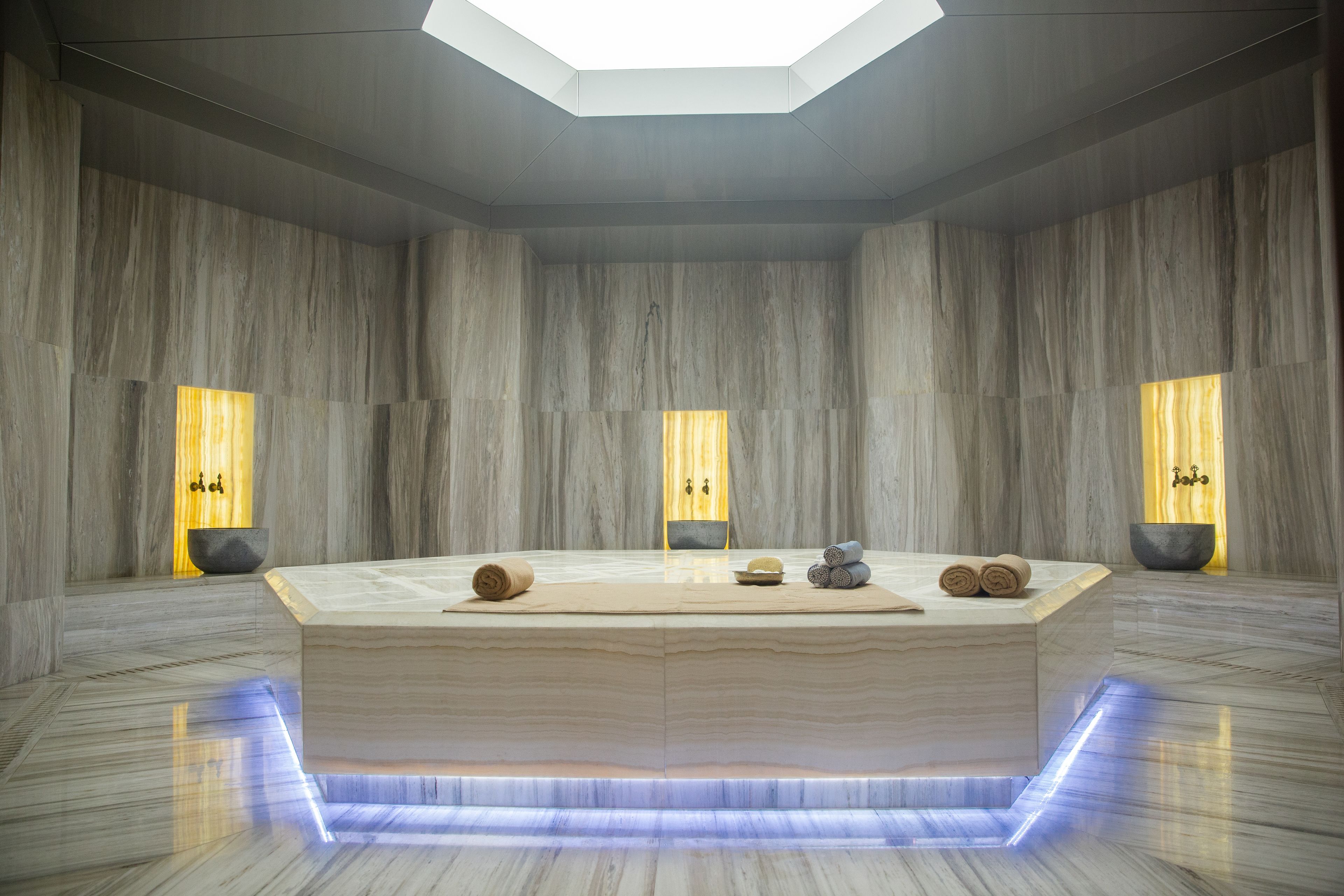 Un área de spa moderna con mostrador de recepción central, paredes de mármol e iluminación ambiental.