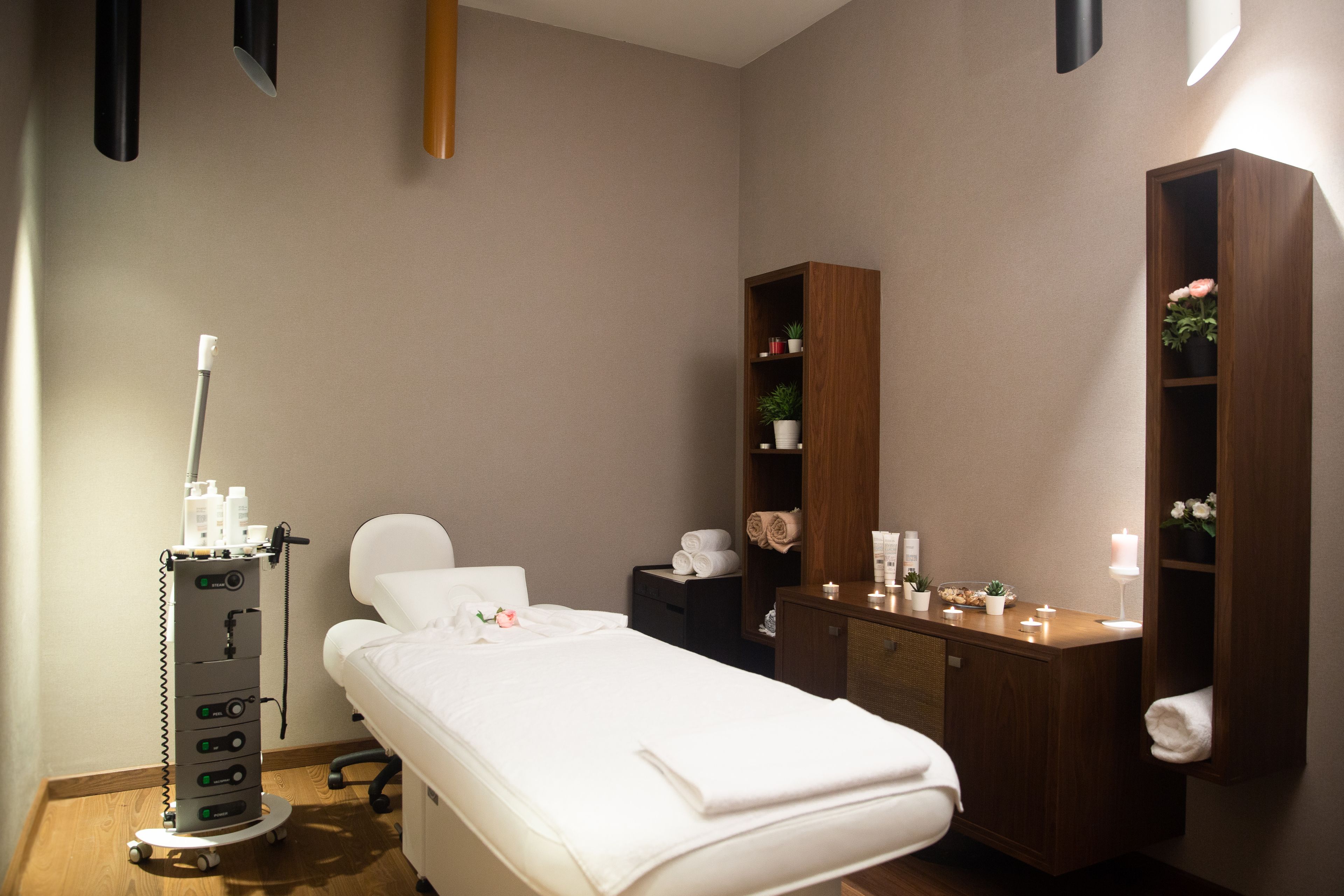 A clean, well-lit room with a single bed, a wooden cabinet with toiletries, and a medical device cart.