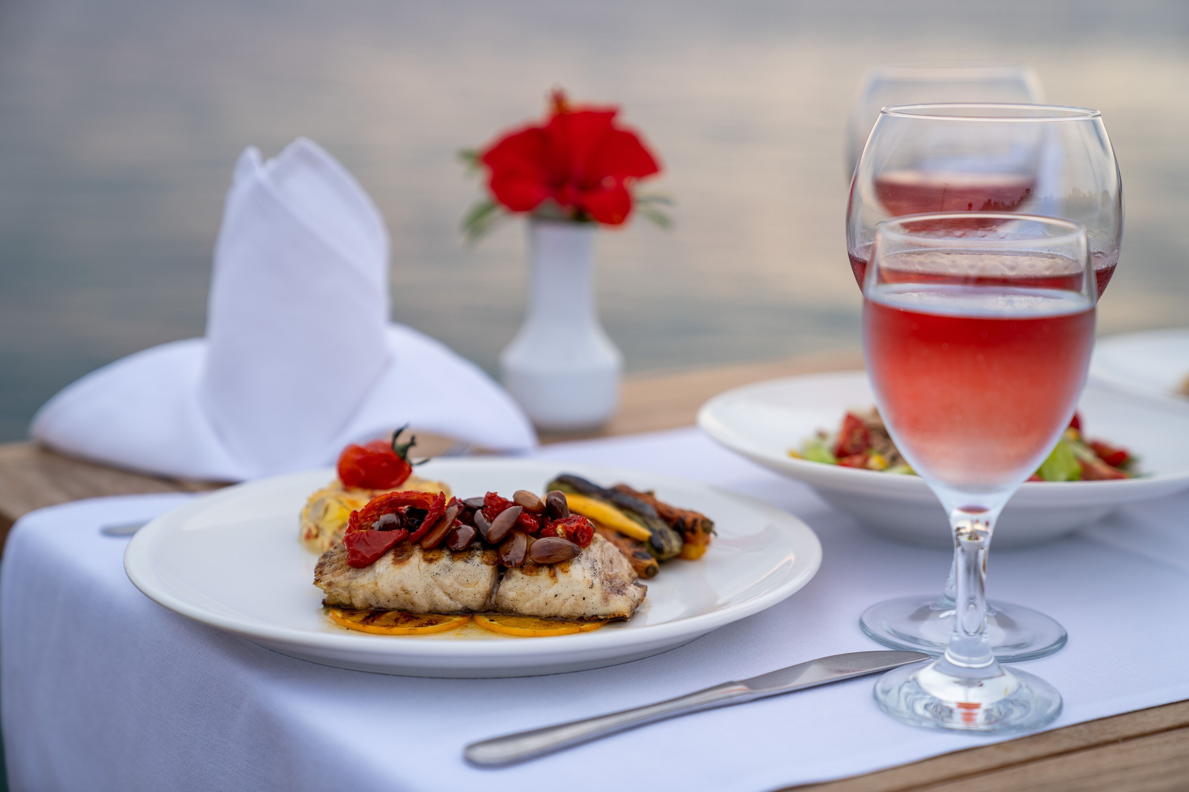 Uma mesa de jantar com toalha branca, um copo de vinho tinto e um prato de comida.