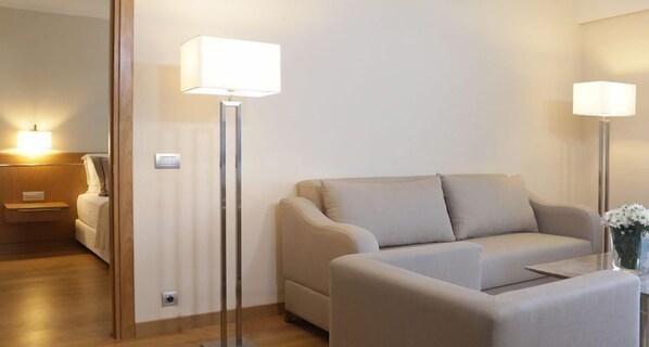 A modern living room with a beige sofa, two floor lamps, and a small table with a vase of flowers. - On'Live Hotel (Cesme)