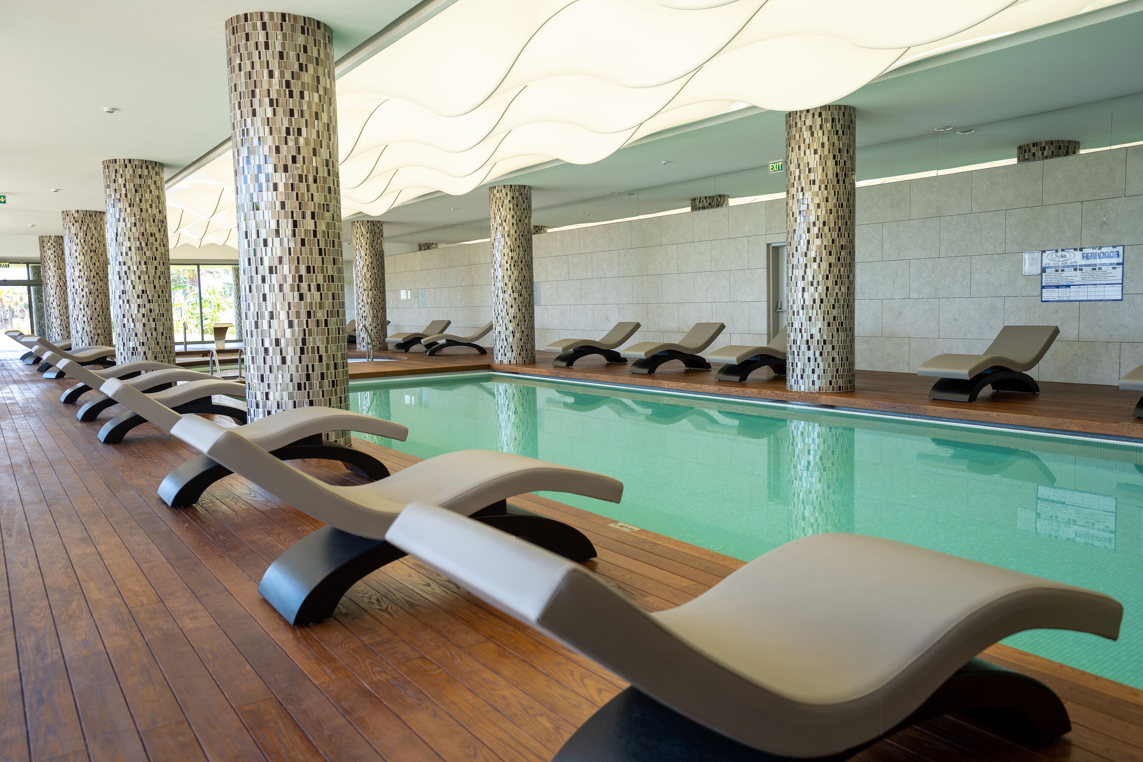 Un área junto a la piscina con sillones de descanso y pilares con diseño.