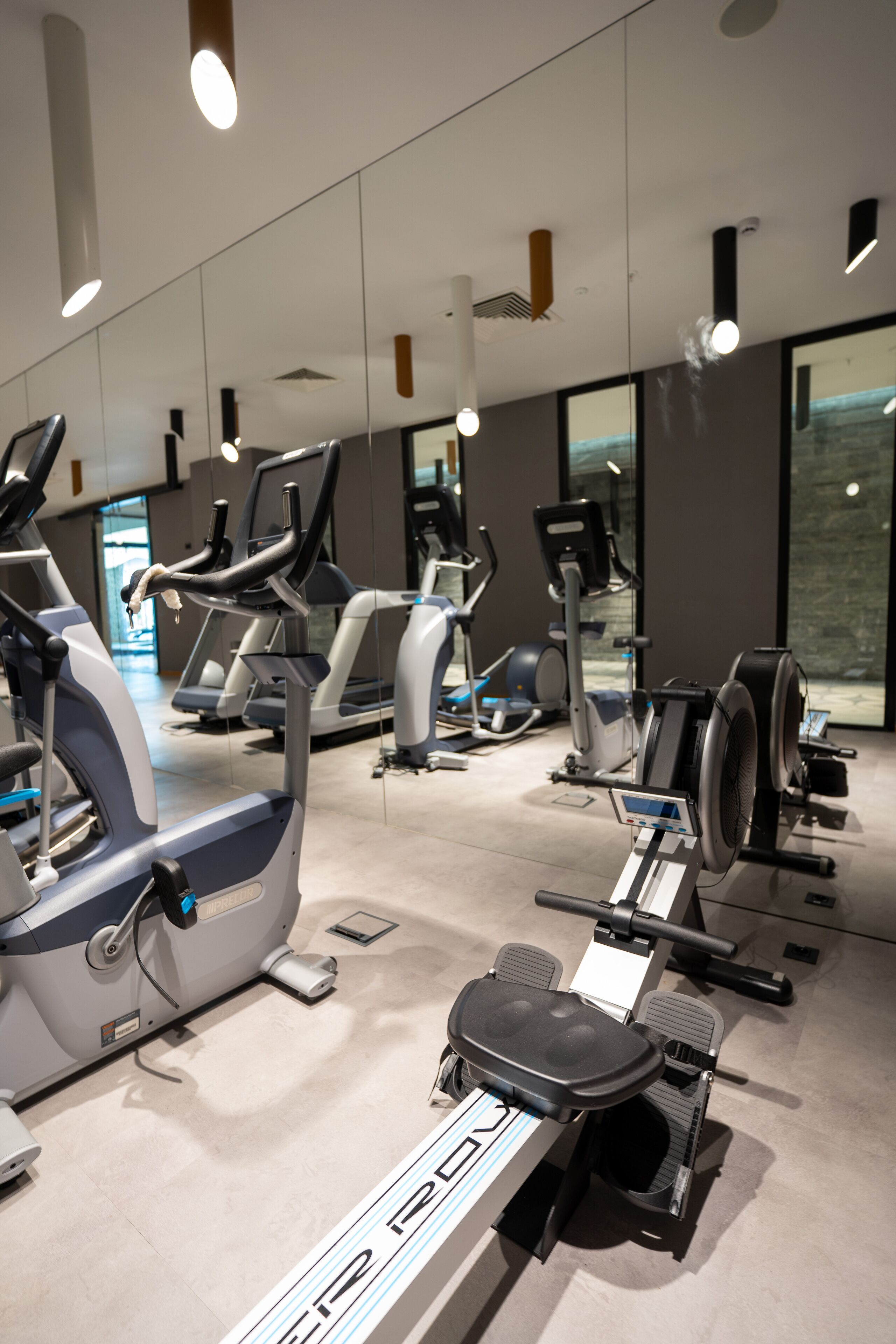 Un gimnasio con varias máquinas de ejercicio, incluyendo cintas de correr y elípticas, dispuestas en un espacio amplio.