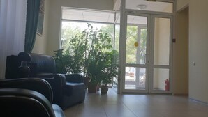 A room with a black leather sofa, a large potted plant, and a sliding glass door leading to an outdoor area. - Altyn-Adam Hotel (Astana)