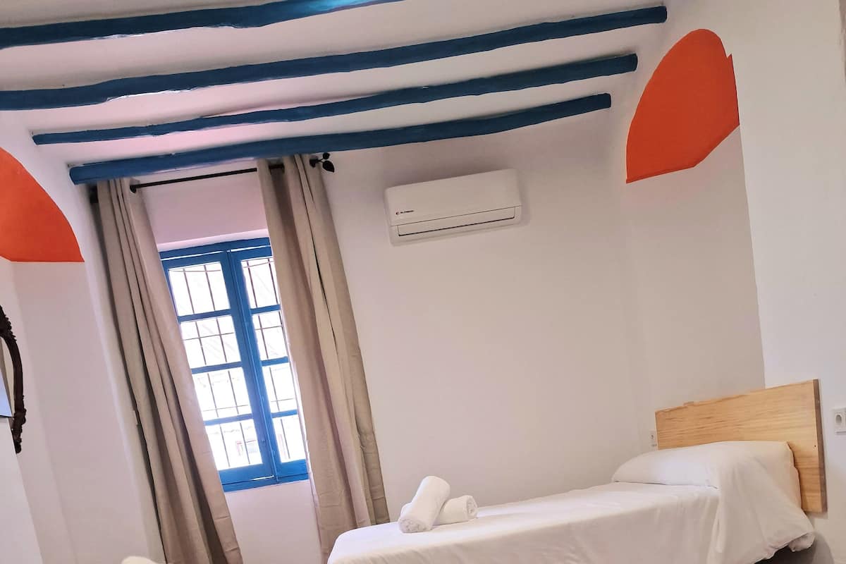 Hotellihuone, jossa on kaksi sänkyä, ikkuna, jossa on verhot, ja seinälle asennettu ilmastointilaite.
