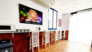 Un'area reception con una TV che mostra un logo colorato, un forno a microonde, un cestino e un pavimento piastrellato.