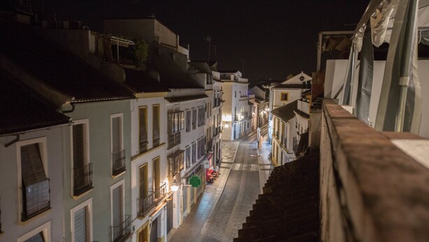 Una vista notturna di una stretta via, fiancheggiata da edifici con balconi e finestre illuminate.