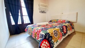 Una camera da letto con un letto, una finestra con tende, un condizionatore d'aria bianco e un pavimento piastrellato.