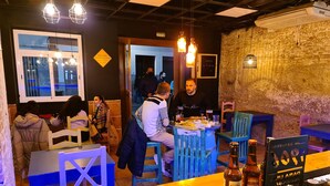 Un interno ristorante con tavoli e sedie in legno, un'area bar con bottiglie e una parete in mattoni.
