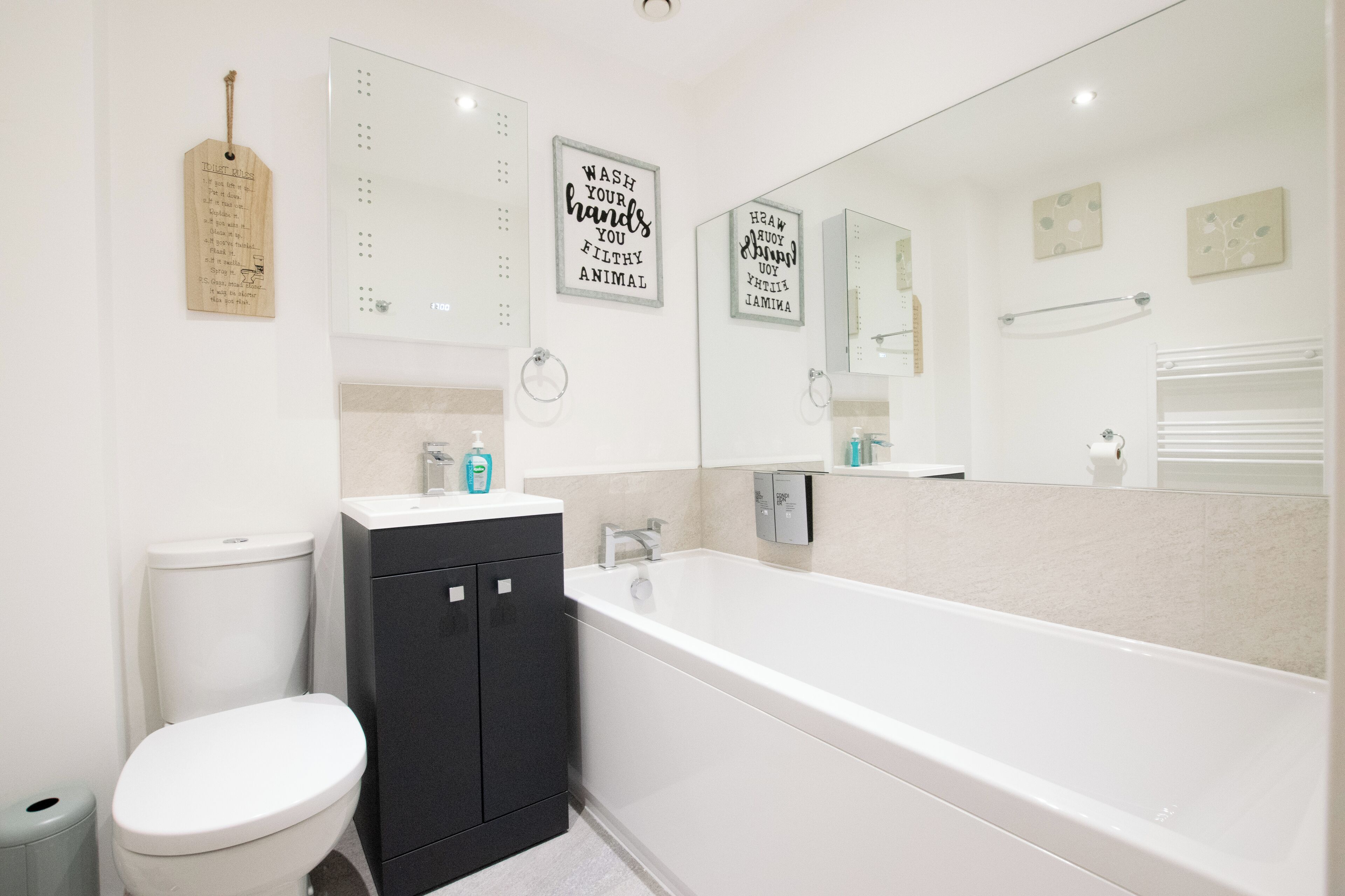 A modern bathroom with a toilet, black cabinet, and a large bathtub.