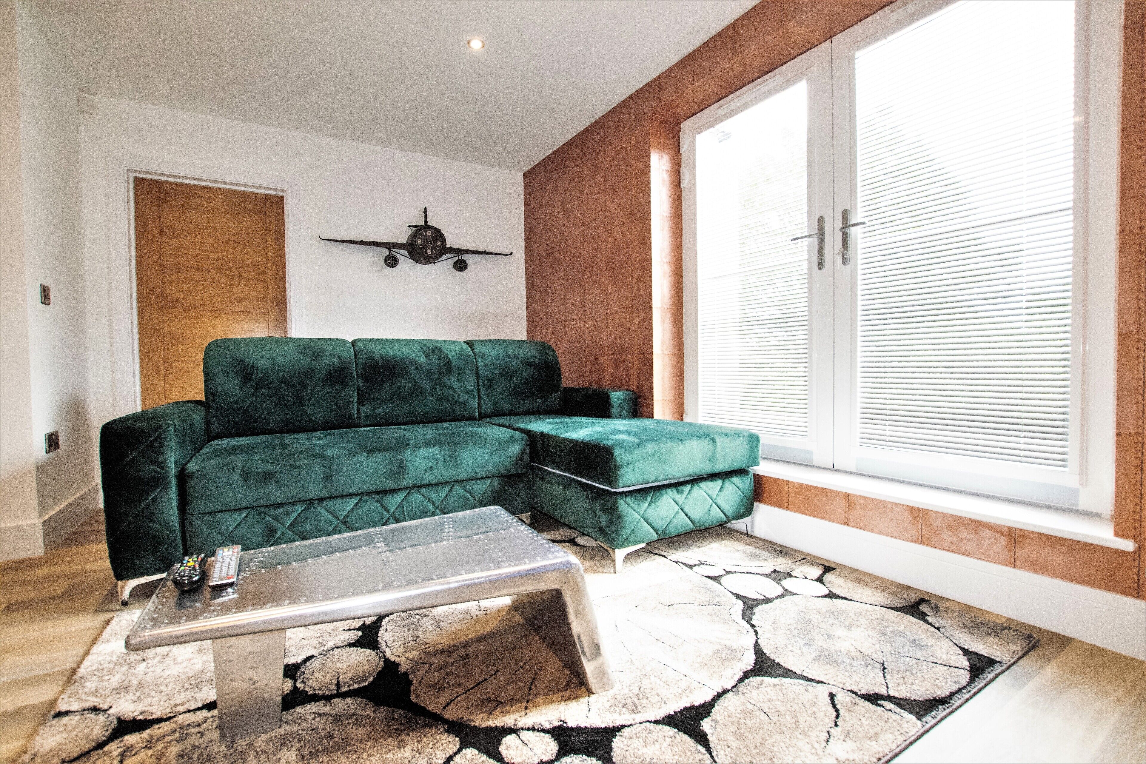 A modern living room with a green sectional sofa, a coffee table, and a large window with blinds.