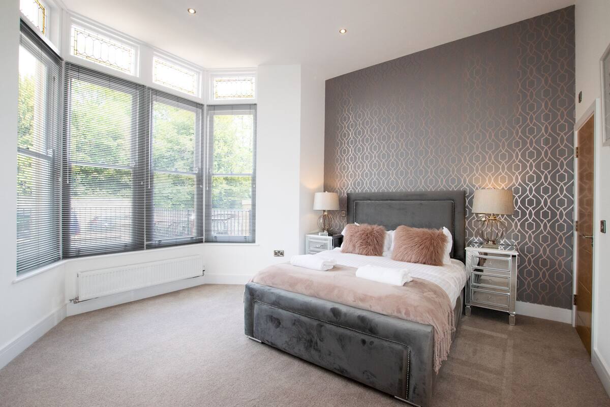 A bedroom with a large bed, two bedside tables, and a patterned wall.