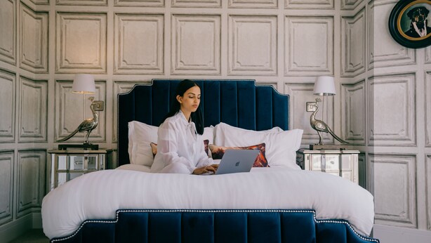A bed with a dark headboard, white bedding, and a laptop on it. There are two bedside tables with lamps and decorative items. - Rowan Tree Your Apartment (Bristol)