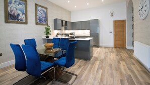 A modern kitchen with a central island, blue chairs around a glass table, and a clock on the wall. - Rowan Tree Your Apartment (Bristol)