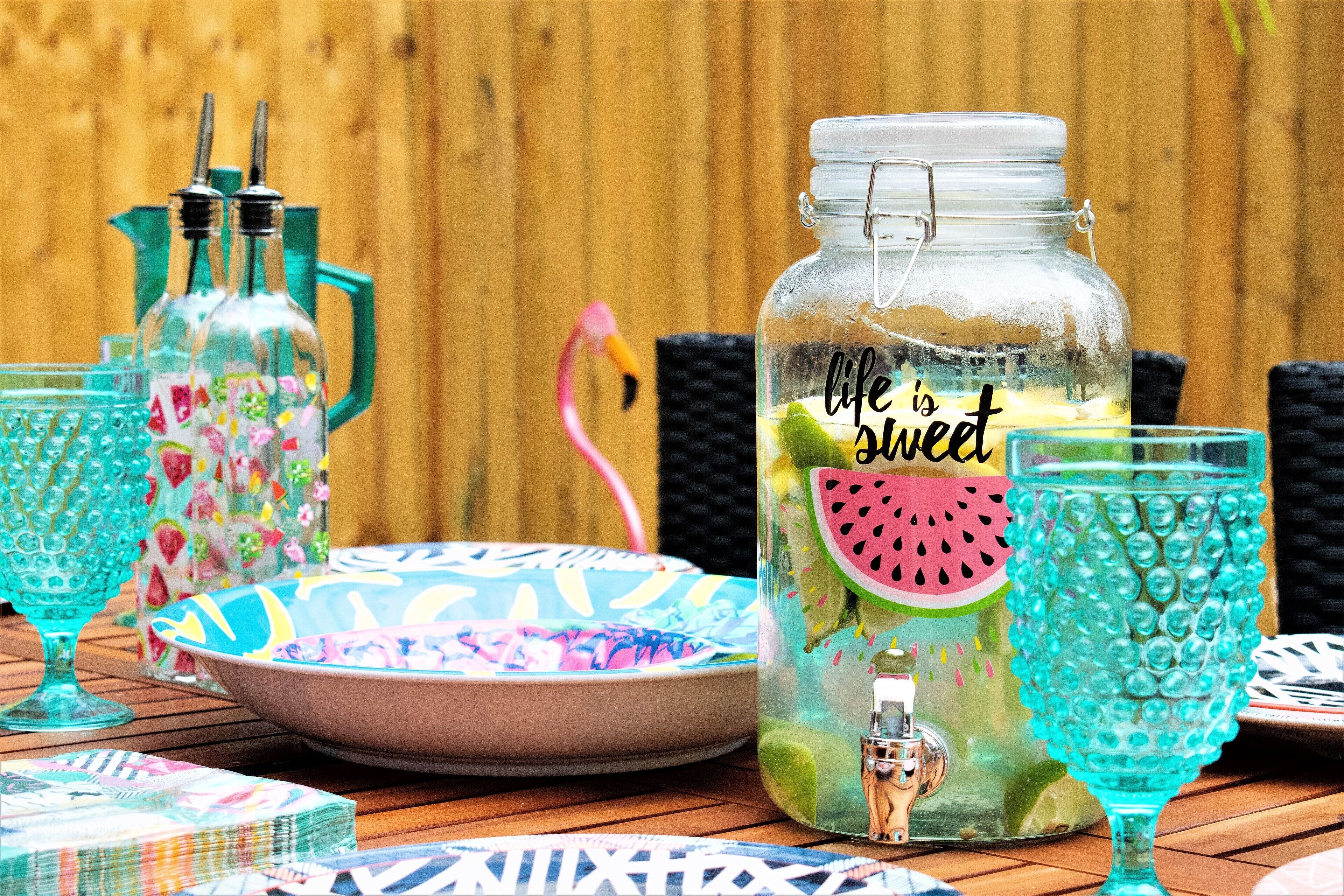 A table with a glass jar labeled "life is sweet" containing lime slices, a pink flamingo, and colorful glassware.