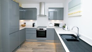A modern kitchen with grey cabinets, a built-in oven, a microwave, and a sink. - Rowan Tree Your Apartment (Bristol)