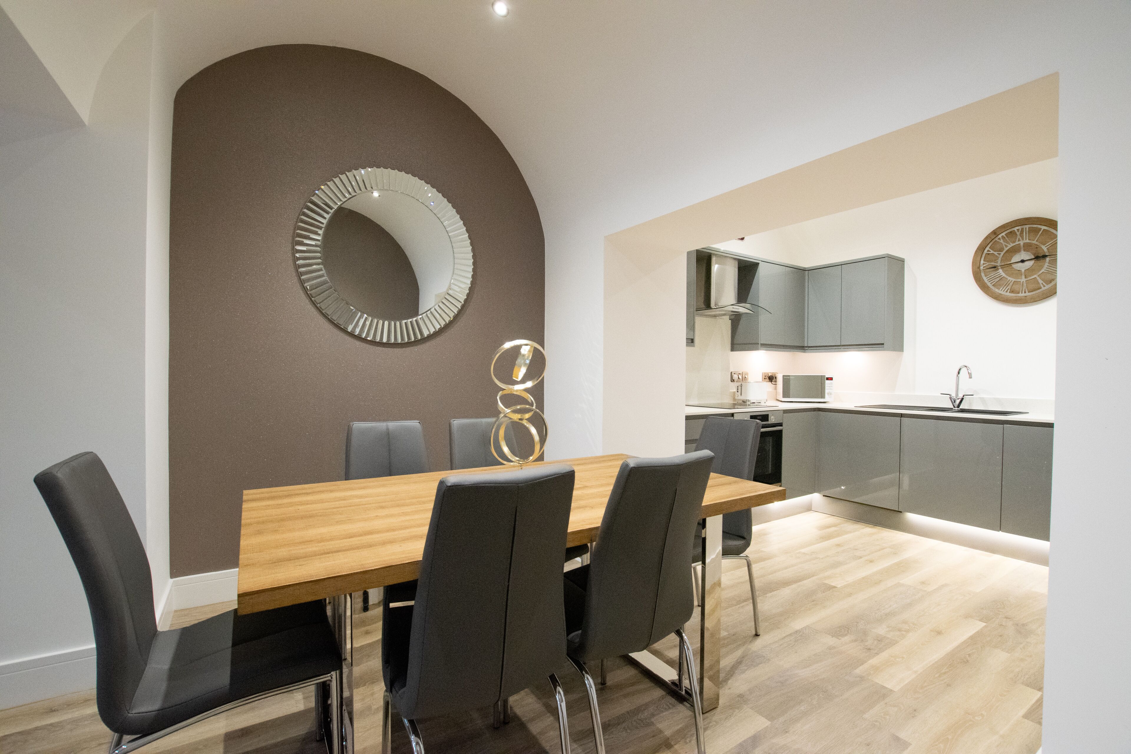 Una cocina moderna con armarios grises, una mesa de comedor de madera y un espejo grande.