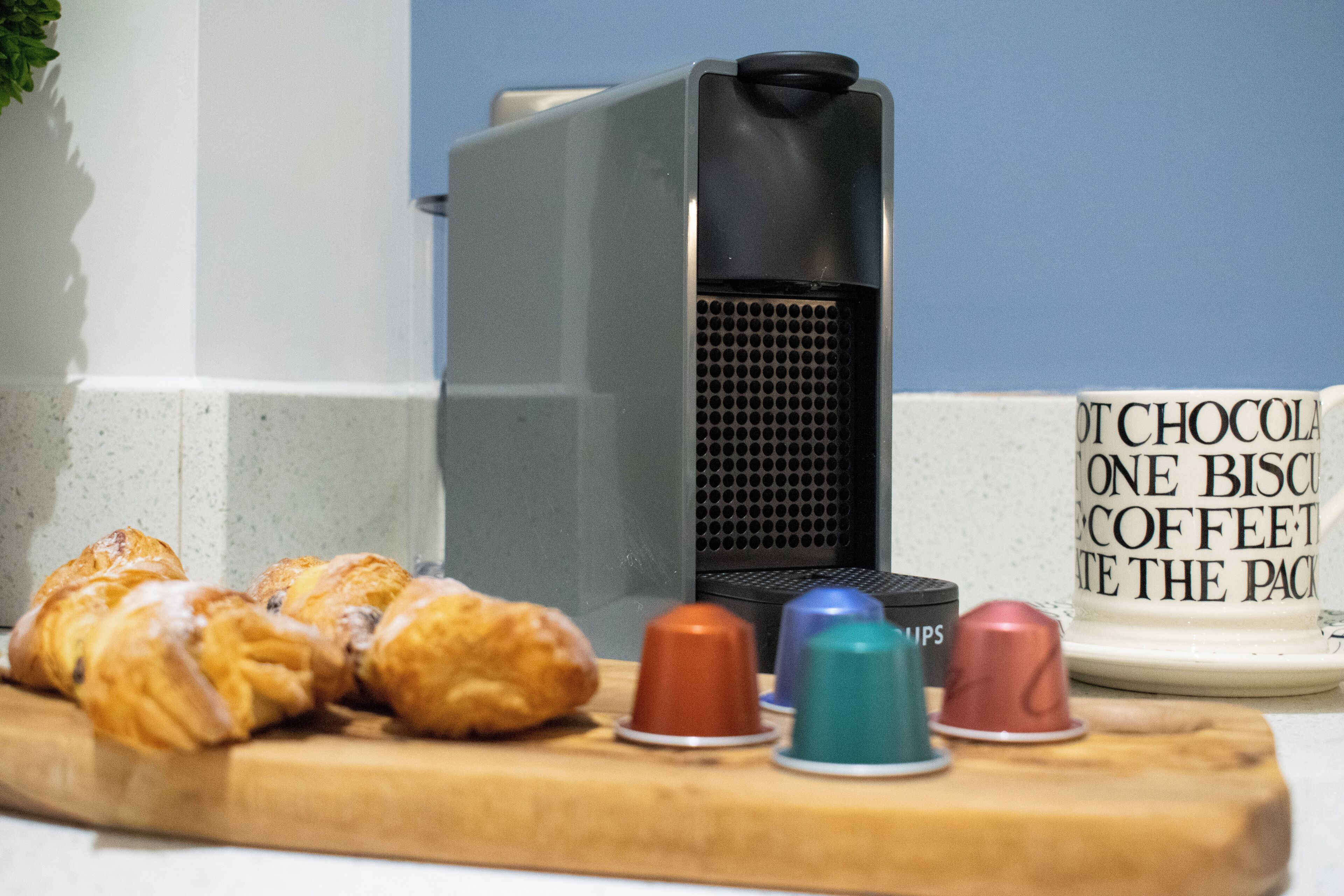 Croissants on a wooden board, a coffee machine, and a mug with text.