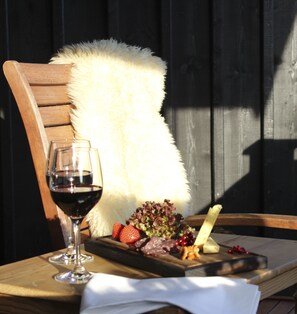 A wooden chair with a white furry cushion, a glass of red wine, and a wooden board with various cheeses, fruits, and a small dish of berries. - Fryksås Hotell & Gestgifveri (Fryksås)