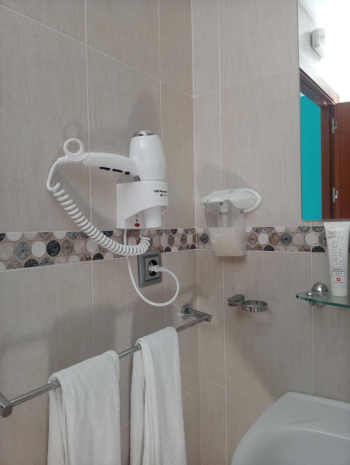 A bathroom with a hairdryer, a towel rack, and a glass shelf with toiletries.