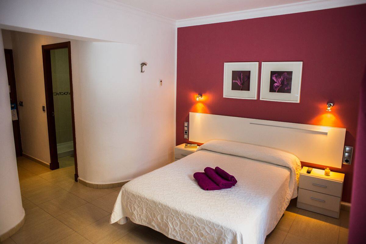 A hotel room with a large bed, two bedside tables, a nightstand, and a door leading to another room.