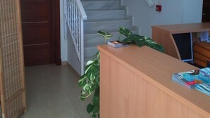 Una zona de recepció amb un taulell de fusta, una escala i una porta.