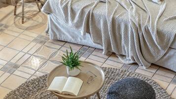 A cozy living room with a sofa, a small round table with a book and a plant, and a large woven rug.