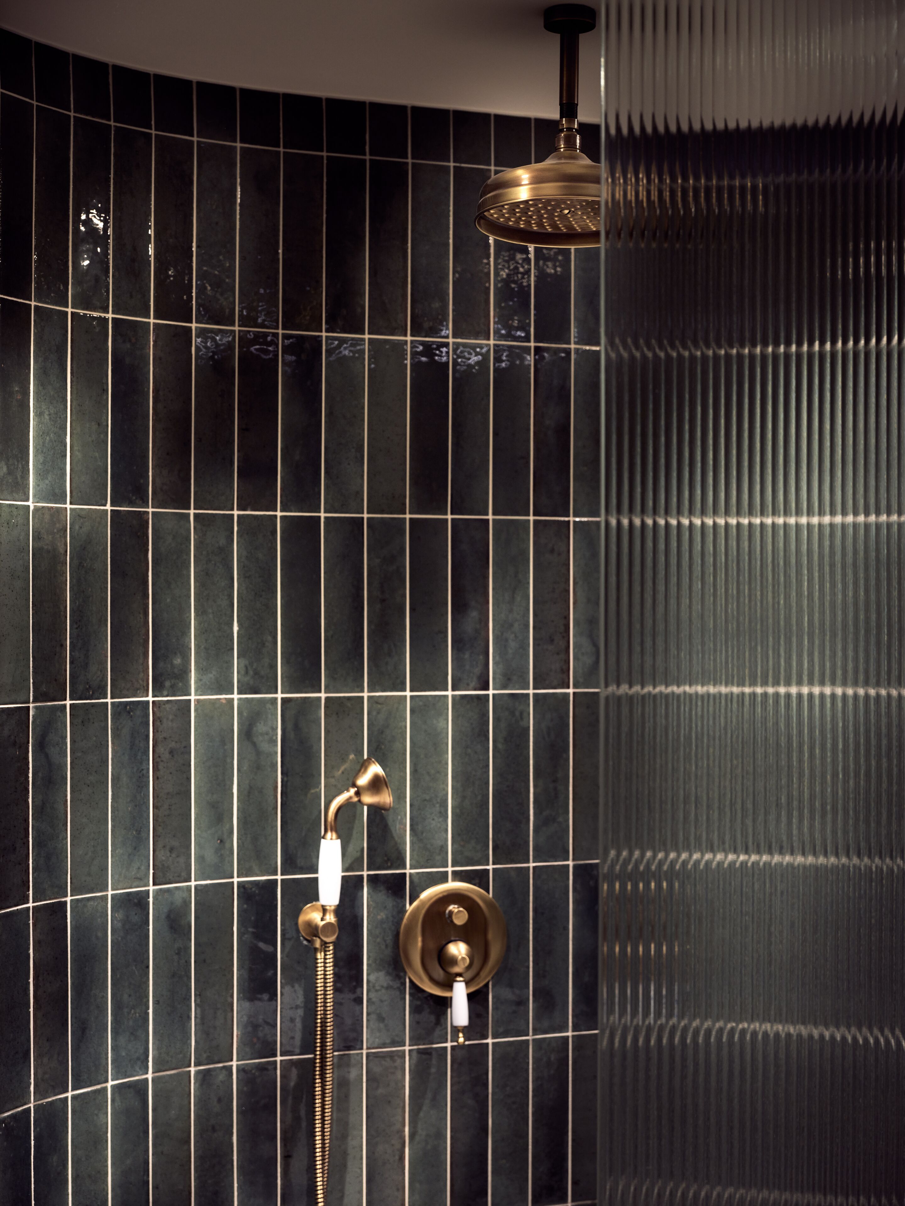 A bathroom with a shower area featuring a curved showerhead and a handheld showerhead.