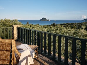 A balcony with wicker furniture, a view of the sea, and a distant island. - Leedas Village (Zakynthos)