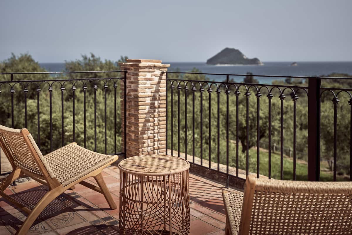A balcony with wicker furniture, a stone pillar, and a view of the sea and an island.