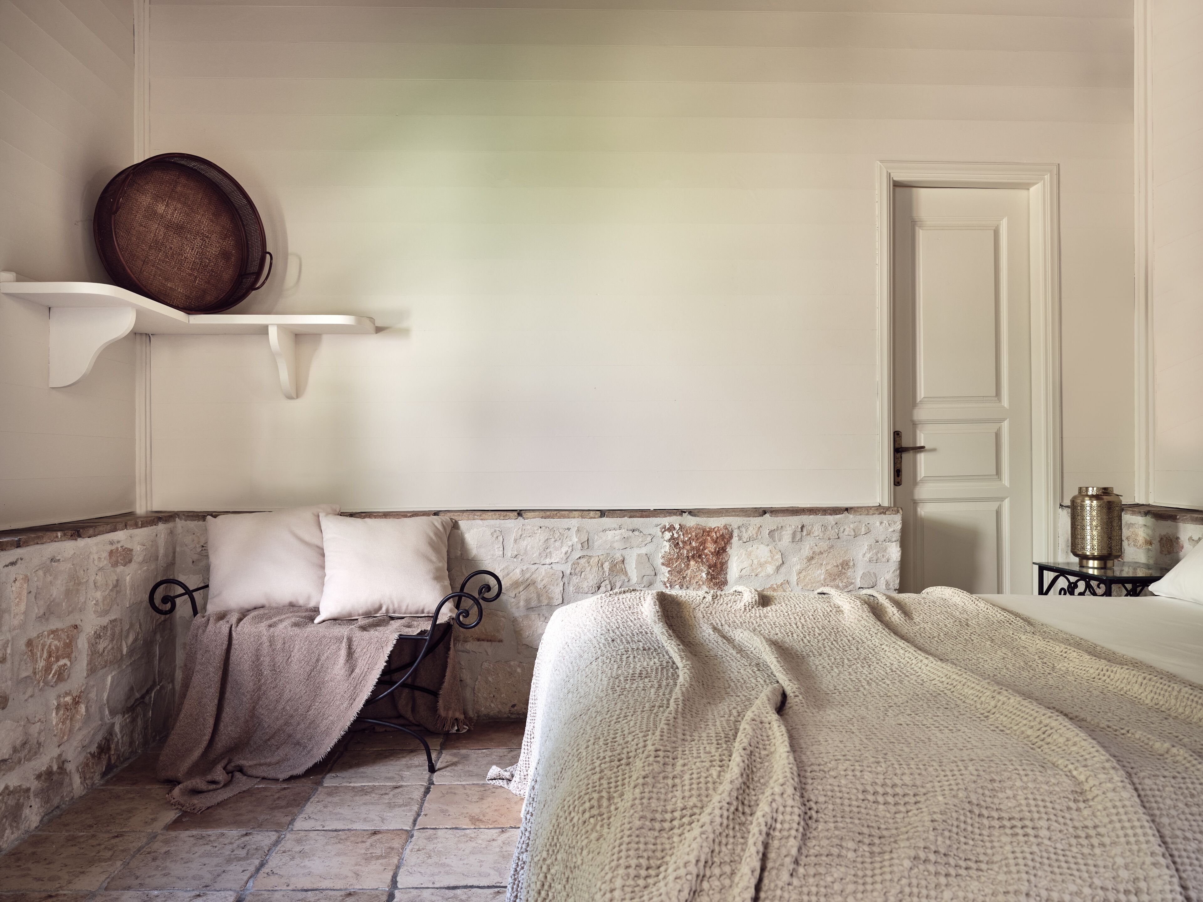 Een kamer met twee bedden, een stenen muur, een witte deur en een plank met een mand.