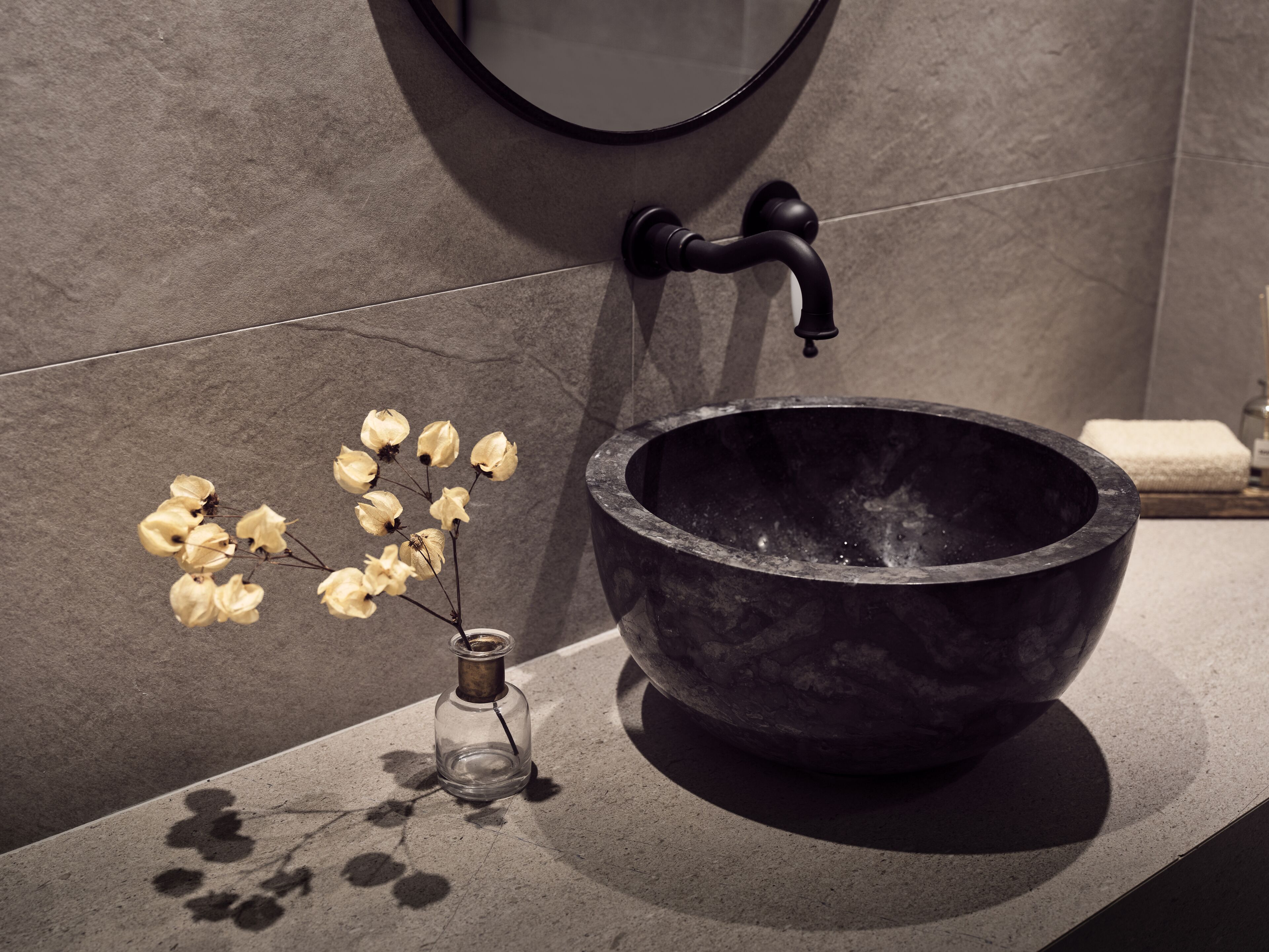 Un baño con un lavamanos de piedra grande, un jarrón pequeño con flores secas y un espejo en la pared.