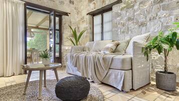 Una sala de estar acogedora con una pared de piedra, un sofá, un reposapiés redondo y una mesita con una planta.