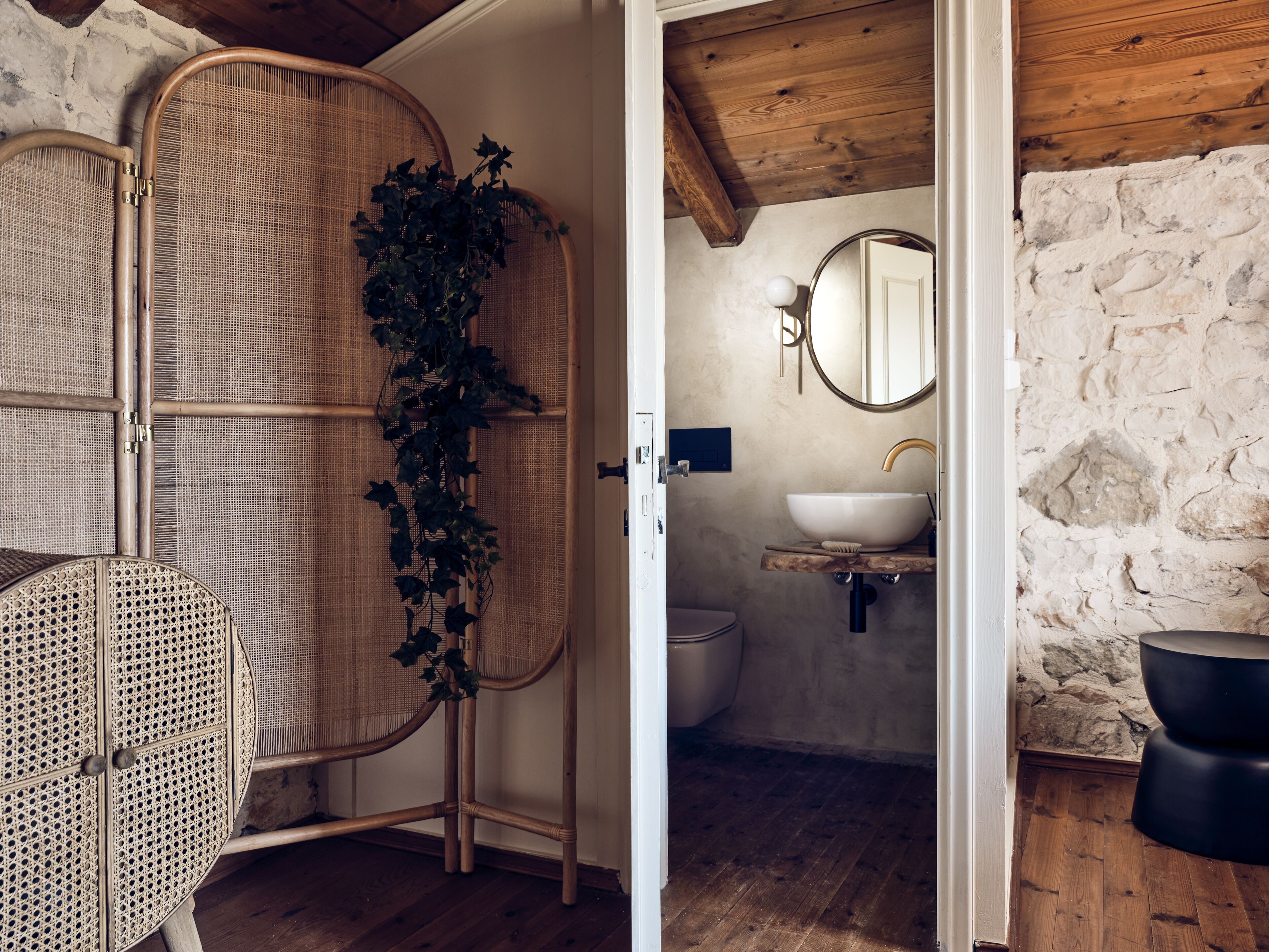 A bathroom with a stone wall, a wooden floor, a white sink, and a mirror.