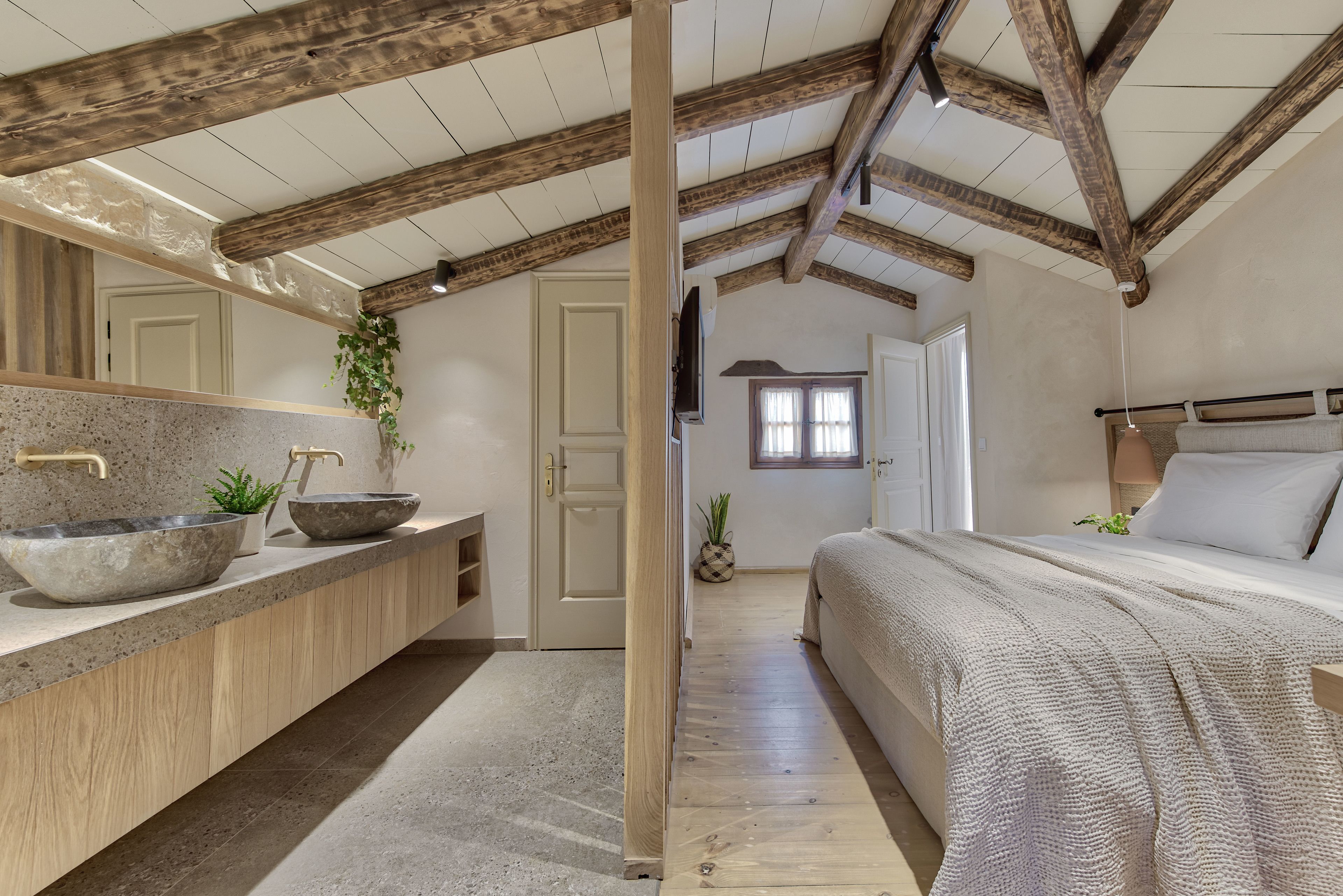 A modern bedroom with a large bed, wooden beams, a stone sink, and a view of the hallway.