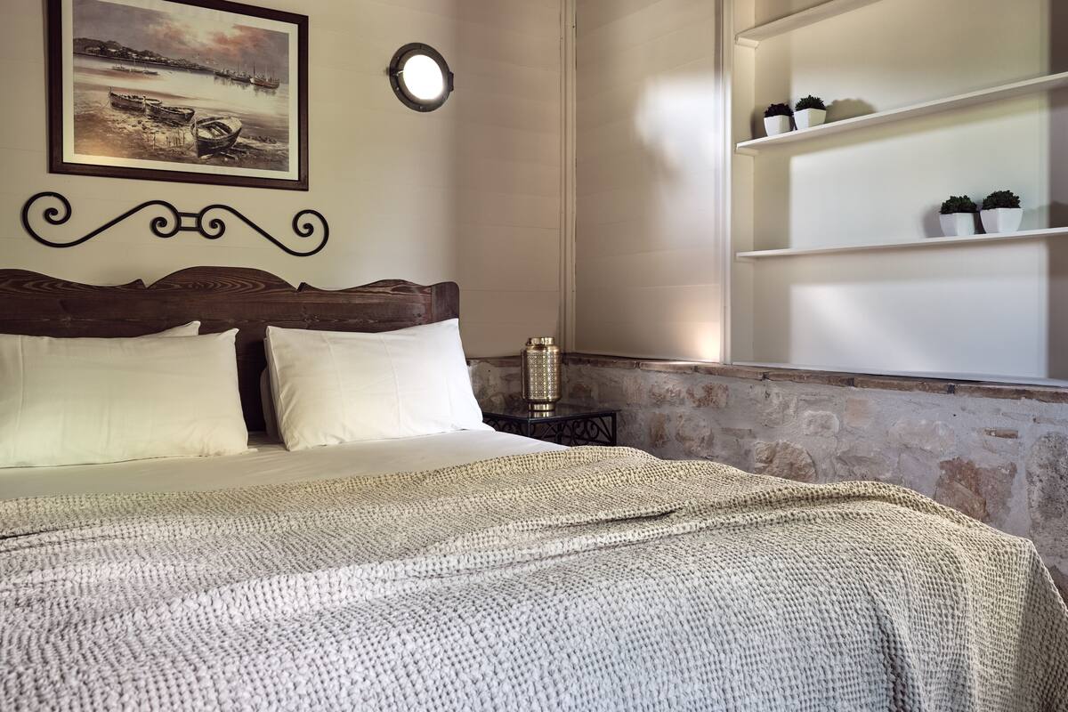 A neatly made bed with white linens, a wooden headboard, and a framed seascape painting on the wall.