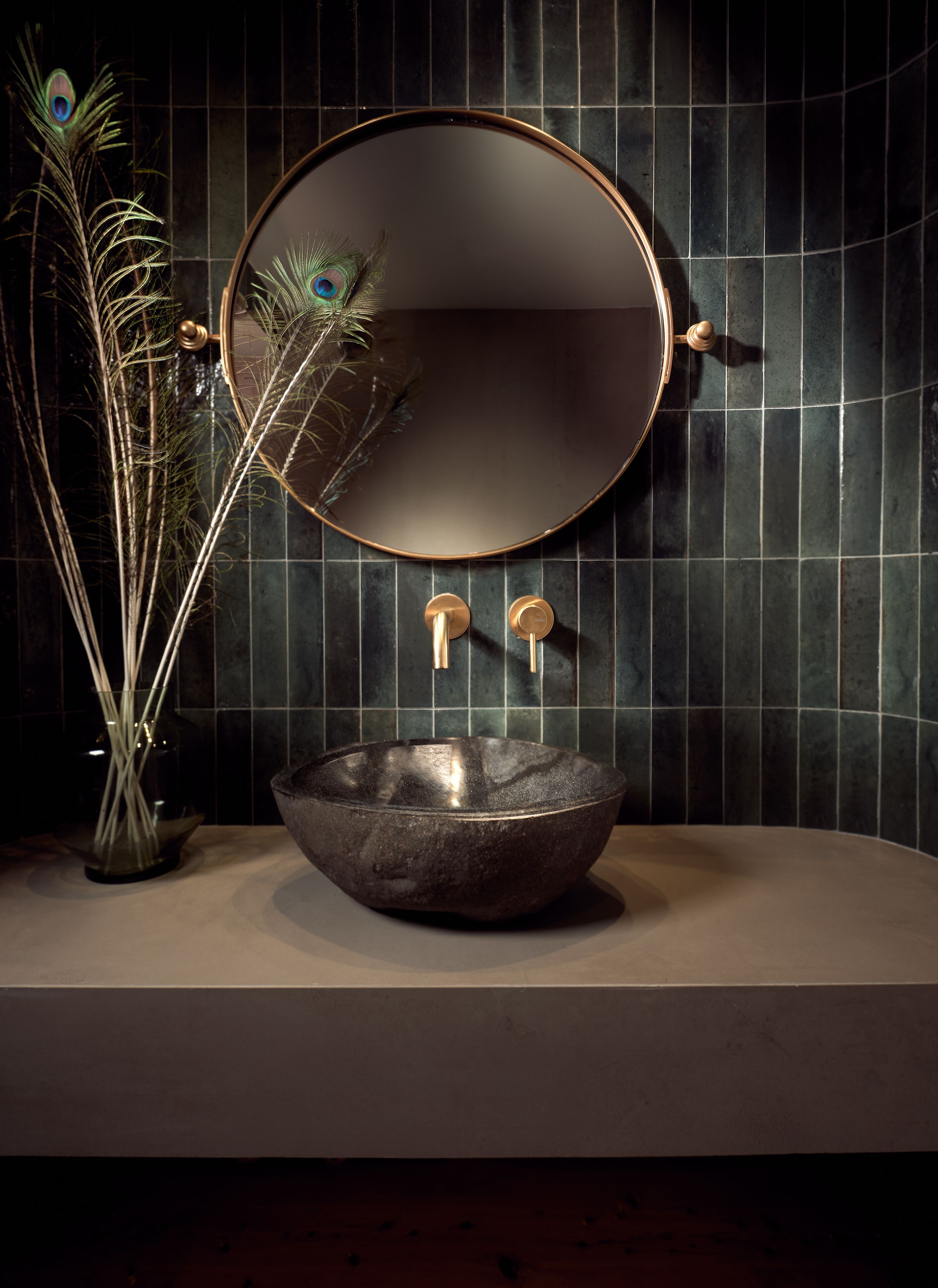 Een badkamer met een ronde spiegel, een wastafel en een decoratie van een pauwenveer.