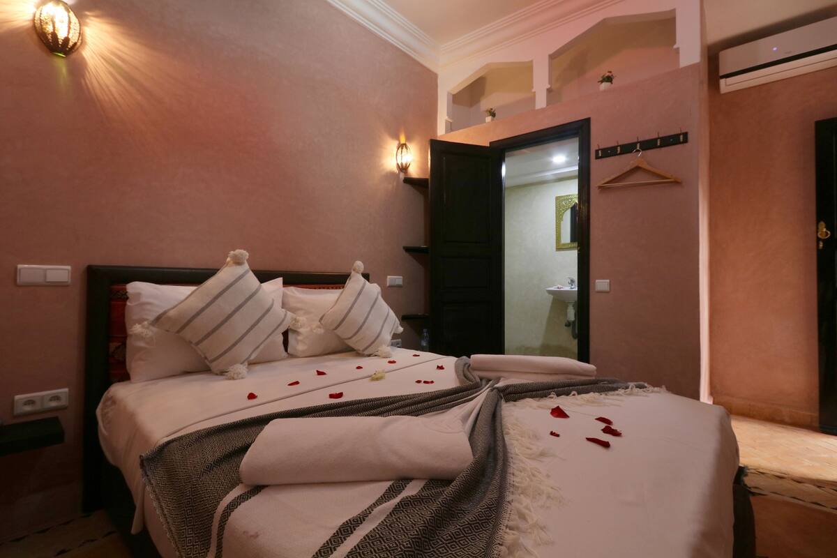 A hotel room with a bed, a nightstand, a mirror, and a wall-mounted light fixture.