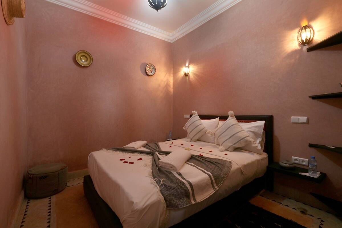 A neatly made bed with pillows and a blanket, a bedside table with a water bottle, and wall sconces.